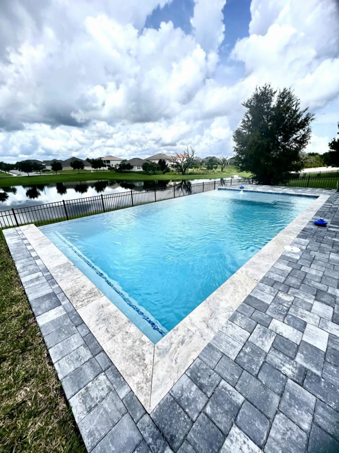 Finished pool by Destiny Renovation: travertine coping, gray pavers and a lake view